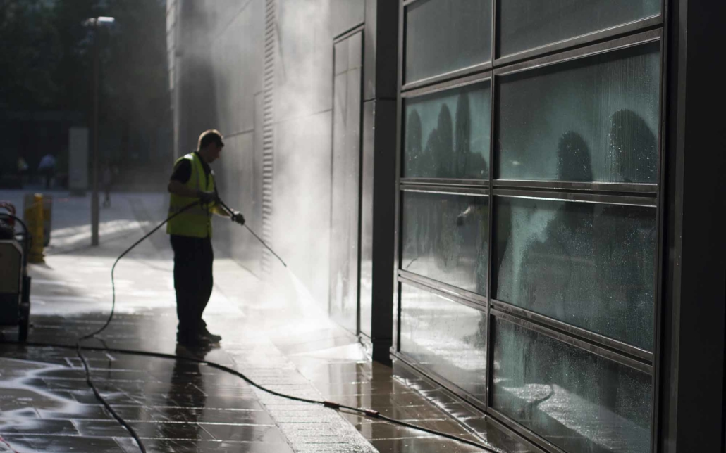 Worker power washing sidewalk and walls