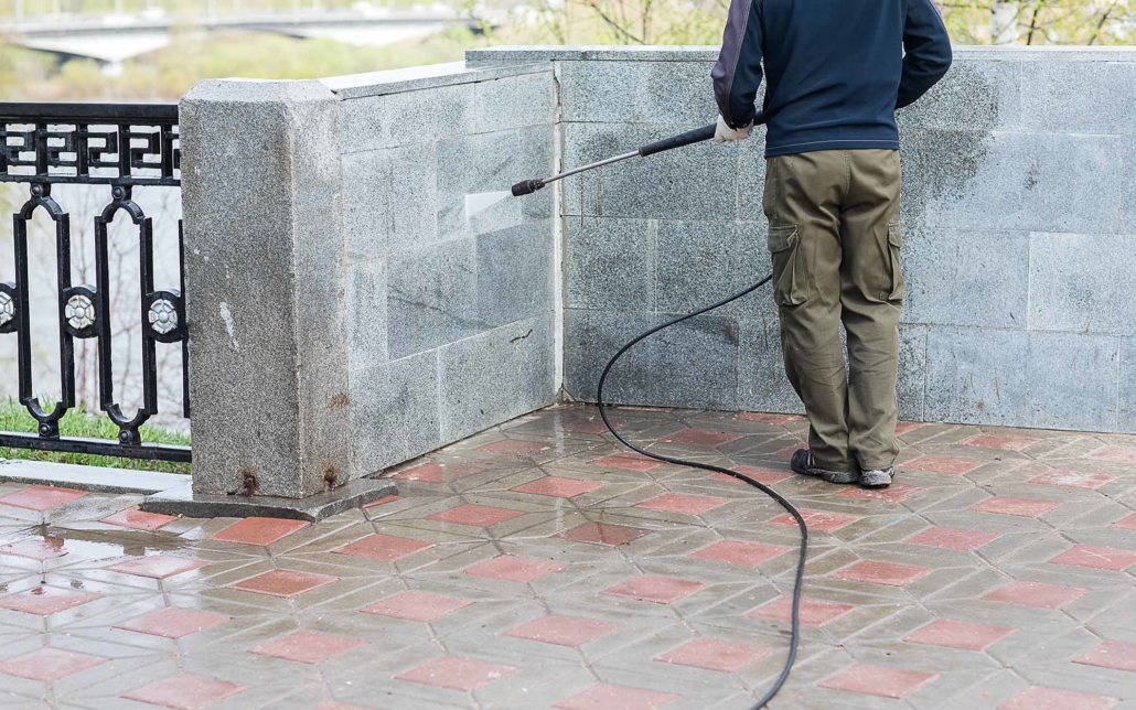 Side view of worker power washing wall