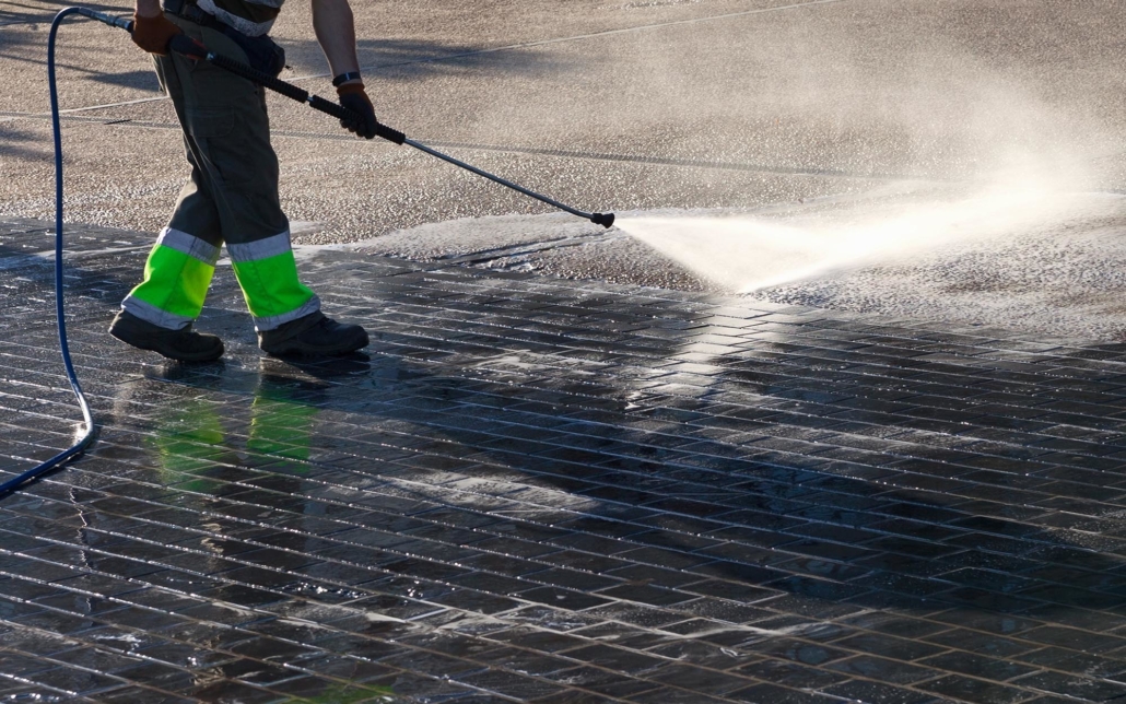Worker using a power washer to clean the sidewalk