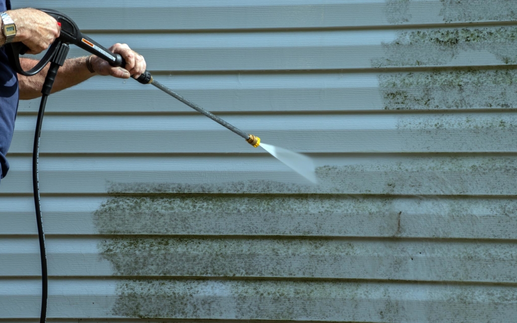 Person using a power washer to clean side of house